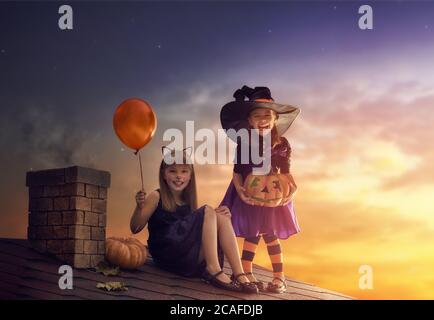 Zwei glückliche Schwestern an Halloween. Lustige Kinder in Karnevalskostümen im Freien. Fröhliche Kinder und Kürbisse auf Sonnenuntergang Hintergrund. Stockfoto