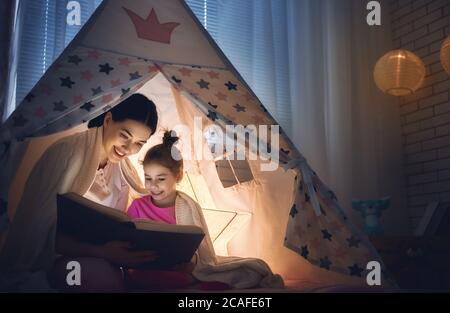 Familie Schlafenszeit. Mutter und Kind Tochter lesen ein Buch im Zelt. Ziemlich junge Mutter und schönes Mädchen mit Spaß im Kinderzimmer. Stockfoto