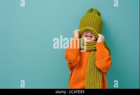 Winterporträt des glücklichen Kindes in Strickmütze, Snood und Pullover. Mädchen, die Spaß, spielen und lachen auf teal Hintergrund. Modekonzept. Stockfoto