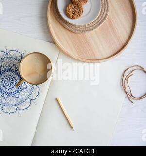 Dekoratives rundes Blumenmandala auf weißem Blatt gezeichnet. Home Entspannung, Hobby und Erholung. Kaffee und Kekse auf weißem Hintergrund. Stockfoto