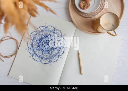 Dekoratives rundes Blumenmandala auf weißem Blatt gezeichnet. Home Entspannung, Hobby und Erholung. Kaffee und Kekse auf weißem Hintergrund. Stockfoto