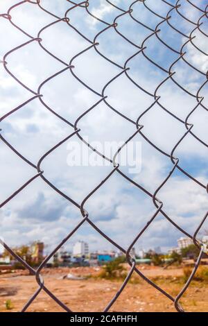 Nahaufnahme alten Eisendraht Zaun Vintage-Netz auf dem Hintergrund der Stadt mit blau bewölkten Himmel. Vertikales Format Stockfoto