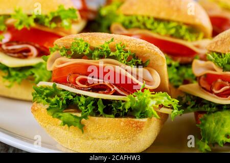 Bunte Sandwiches mit Schinken, Gemüse und Käse auf weißem Teller auf Holzhintergrund. Nahaufnahme. Stockfoto