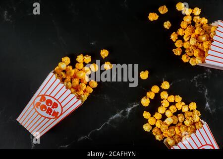 Gelbes Popcorn in gestreiften Schachteln auf schwarzem Hintergrund verschüttet. Stockfoto