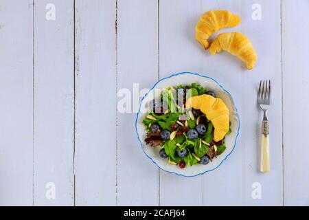 Frühlingsgrüner Salat mit Heidelbeere, Preiselbeere, gerissener Mandel und Croissant auf Holztisch. Stockfoto