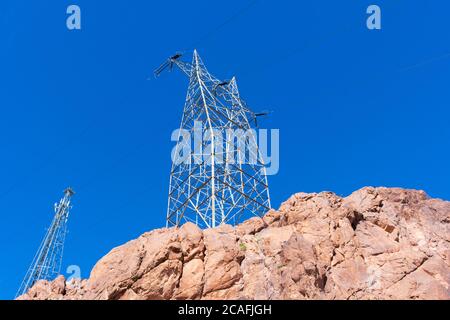 Hochspannungstürme mit parallelen Linien auf der Spitze des felsigen Hügels in den blauen Himmel. Stockfoto