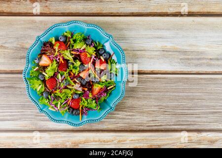 Gemischter Salat mit Beeren, grünen Blättern, Karotte, Heidelbeere und Mandel auf blauem Teller. Stockfoto