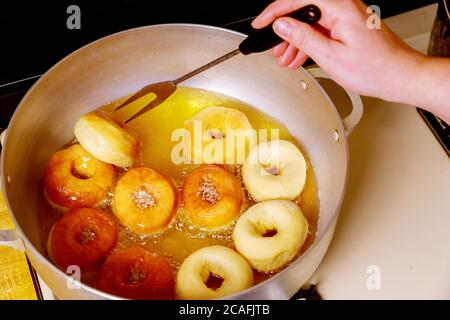 Frau dreht und fritiert runde Donuts mit Loch in heißem Öl. Stockfoto