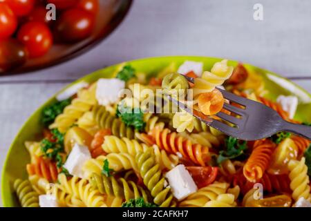 Rotini Pasta und Kirschtomate mit grünem Salat auf Holztisch mit Gabel. Stockfoto