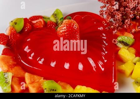 Herzförmige Gelatine mit frischer Erdbeere, Kiwi und Ananas verziert. Dessert zum Valentinstag. Stockfoto