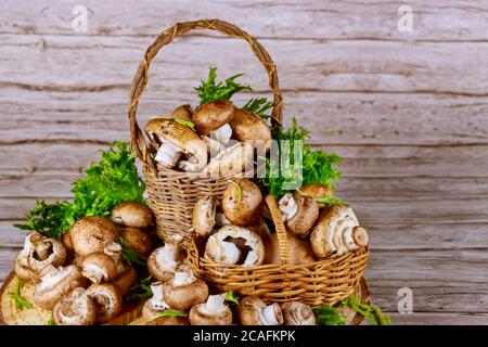 Korbkörbe voll mit frischen braunen Champignon-Pilzen auf Holzgrund. Stockfoto