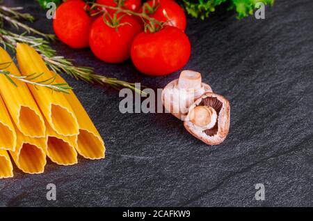 Ungekochte Hartweizen-Pasta mit frischen Tomaten und Pilzen auf dunklem Hintergrund. Stockfoto