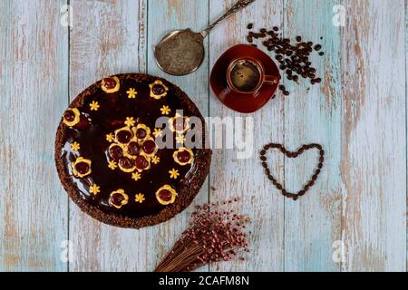 Kirschkuchen mit Schokoladenglasur, Tasse Kaffee und Blumen auf Holzgrund. Stockfoto
