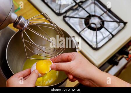 Frau bricht das Ei in eine Rührschüssel und trennt Eiweiß von Eigelb. Biskuitkuchen machen. Stockfoto