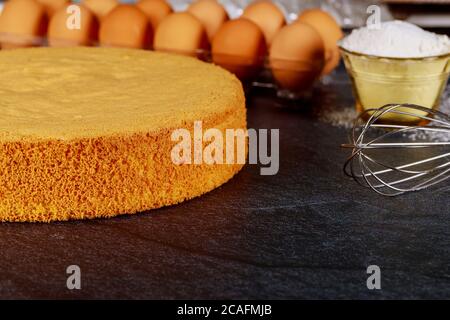 Hausgemachter Biskuitkuchen und Schneebesen mit Zutaten: Eier, Mehl. Stockfoto