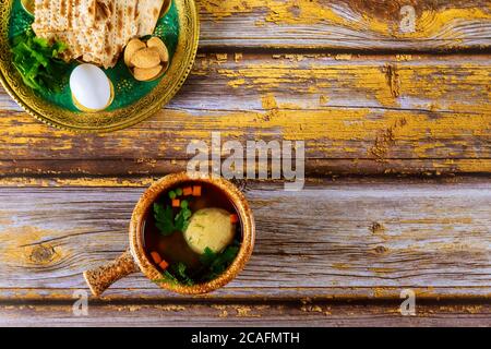 Traditionelle jüdische Matzoballsuppe und Sederteller auf Holztisch für Passah. Stockfoto