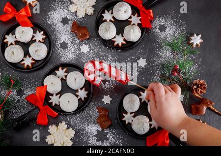 Weihnachtliche Dekoration mit zuckergepuderten Donuts in Skillets. Die Hand der Kinder nimmt Süßigkeiten vom Tisch. Stockfoto