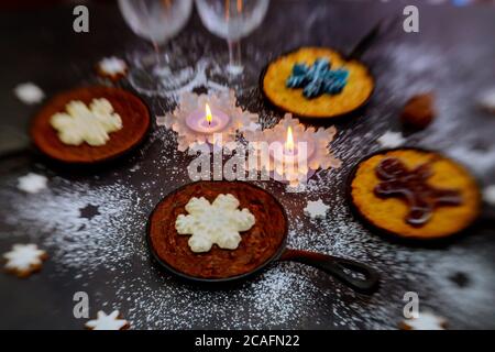 Weihnachts-Esstisch mit brennenden Kerzen, Gläsern und vier Mini-Kuchen mit Dekoration. Stockfoto