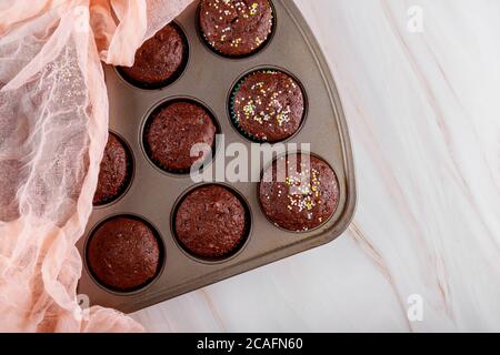 Gebackene Schokoladen-Muffins mit farbigen Streuen in Backform. Stockfoto