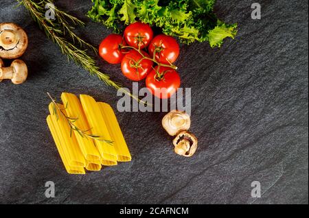 Bio Pasta Manicotti mit Pilzen und Tomaten auf schwarzem Hintergrund. Stockfoto