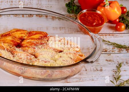 Besetztes Jumbo Shells Pasta in Glasbackpfanne auf weißem Holz Hintergrund. Stockfoto