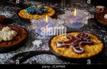 Weihnachts-Esstisch mit brennenden Kerzen, Gläsern und vier Mini-Kuchen mit Dekoration. Stockfoto