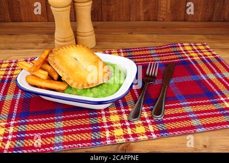 Steak und Kidney Pie und Chips Mahlzeit mit matschigen Erbsen In einer Metall-Emaille-Schale Stockfoto