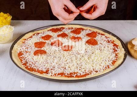 Der Koch legt geschnittene Pepperoni auf rohen Pizzateig. Stockfoto