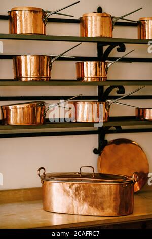 Große längliche Pfanne auf der Arbeitsplatte mit Schöpfkellen und Kochtöpfen aus Kupfer auf den Regalen, in verschiedenen Größen auf massiven Metallregalen, befestigt Stockfoto