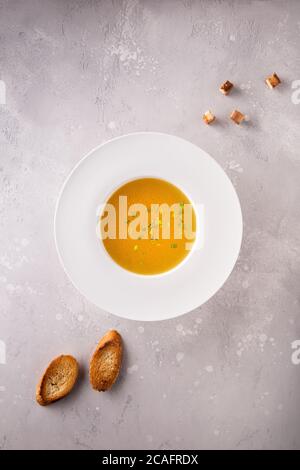 Hühnerbouillon mit gehackten grünen Zwiebeln in weißem Hutteller, einigen Croutons und geröstetem Baguette. Flach legen auf grau strukturierten grauen Stein Hintergrund. Cop Stockfoto