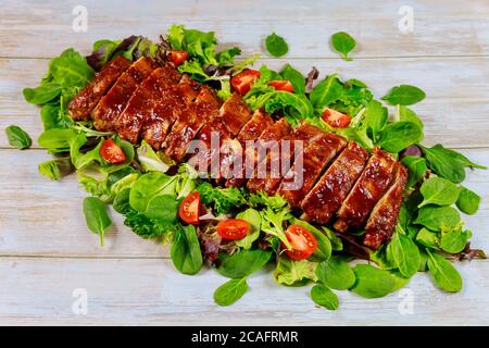 Gebackene saftige Grillrindrippen mit BBQ-Sauce und Salat auf Holztisch. Stockfoto