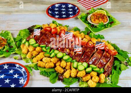 Leckeres Grillfleisch mit Gemüse auf Partytisch mit amerikanischen Mustertellern. Stockfoto