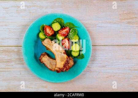 Schweinebrippen mit BBQ-Sauce und Gurken mit Tomate auf blauem Teller. Stockfoto
