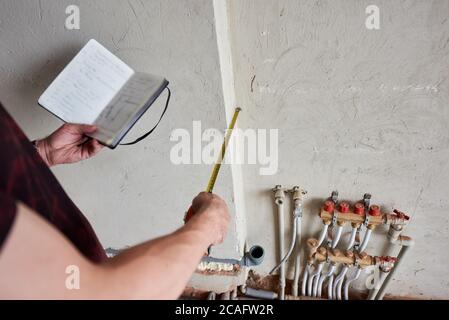 Nahaufnahme der männlichen Hände, die das Notebook mit Bauplan und Maßband halten. Mann nimmt Messung während der Arbeit an der Renovierung der Wohnung. Konzept der Reparatur und Sanierung. Stockfoto