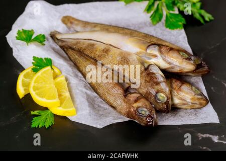 Ganzer frischer Fisch auf Pergamentpapier mit Zitrone und Petersilie. Meeresfrüchtekonzept. Stockfoto