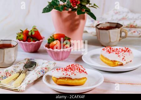 Tee-Party-Tisch mit herzförmigen Donuts, Erdbeere und Vase mit roter Rose. Stockfoto