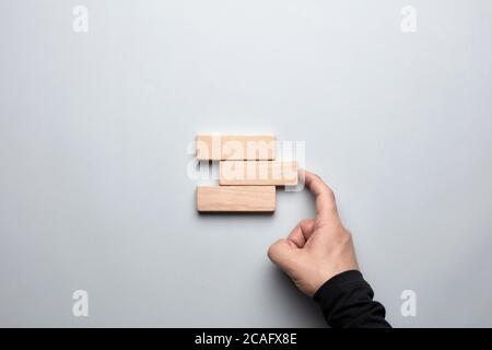 Männliche Hand, die den Spalt zwischen den Holzklötzen vervollständigt. Konzept, um ein Ziel zu erreichen oder eine Lösung im Geschäft zu finden. Stockfoto