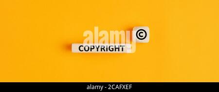 Das Wort Copyright und Copyright-Symbol auf Holzblöcken auf gelbem Hintergrund. Konzept der Patentierung oder des Urheberschutzes. Stockfoto