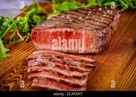 Gegrilltes, seltenes Rindersteak mit Rucola auf Holzbrett. Stockfoto