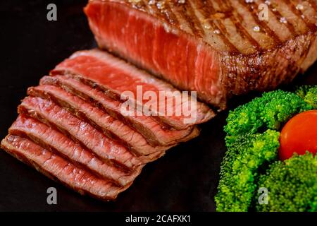 In Scheiben geschnittenes, seltenes Rinderfilet mit Brokkoli auf schwarzem Hintergrund auf Holztisch. Stockfoto