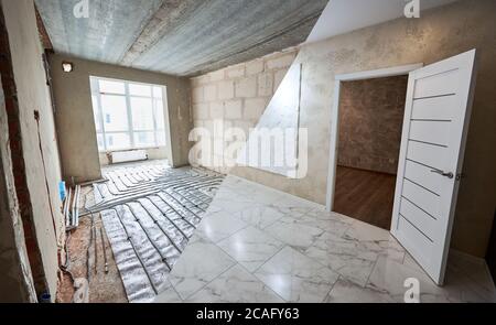Vergleich der neu renovierten Zimmer mit offener Tür und alten Ort mit großen Fenster und Fußbodenheizung Rohre. Moderne Wohnung vor und nach der Restaurierung. Konzept der Hausrenovierung. Stockfoto