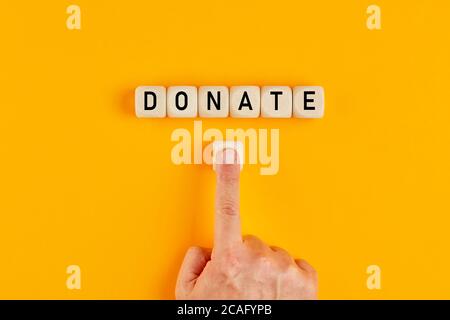 Das Wort Donate auf Holzwürfeln geschrieben mit einer männlichen Hand drücken Sie den Knopf für die Spende. Wohltätigkeitskonzept. Stockfoto