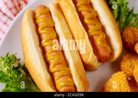 Hot Dog mit Senf auf weißem Teller mit Salat. Nahaufnahme. Stockfoto