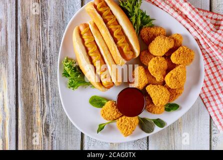 Panierte Hähnchennuggets mit Ketchup und Hot Dog mit Senf auf weißem Teller. Fast-Food-Konzept. Stockfoto