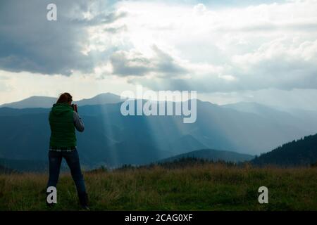 Mädchen Fotografin in den Bergen schießt die Landschaft auf der Hintergrund der Sonnenstrahlen an einem bewölkten Tag Stockfoto