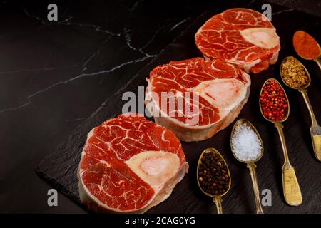 Frisch geschnittenes Rindsstück und Würze in Löffeln auf schwarzem Brett. Stockfoto