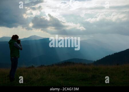 Mädchen Fotografin in den Bergen schießt die Landschaft auf der Hintergrund der Sonnenstrahlen an einem bewölkten Tag Stockfoto