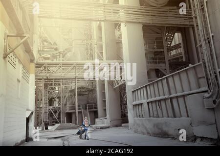 Ein asiatischer Mann, der eine Schubkarre in einer dunklen schmutzigen Fabrik zieht. Konzentrieren Sie sich auf einen Arbeiter. Arbeiten Sie hart Konzept. Stockfoto