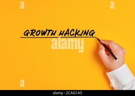 Männliche Hand schreibt das Konzept des Wachstums Hacking auf gelbem Hintergrund. Growth Hacking impliziert ein massives Wachstum in kurzer Zeit mit einem kleinen Budget in Stockfoto