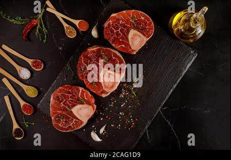 Rohes Rindsschenkel und Gewürze für die Zubereitung von Ossobuco auf schwarzem Hintergrund. Draufsicht. Stockfoto